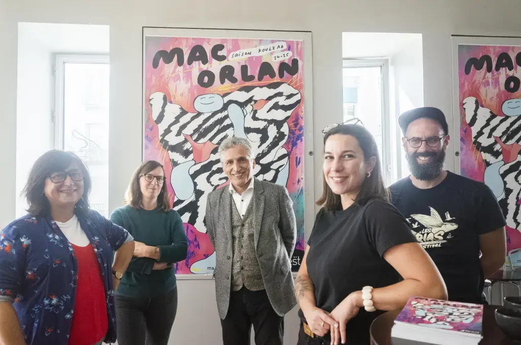 Cinq personnes posent devant une affiche.