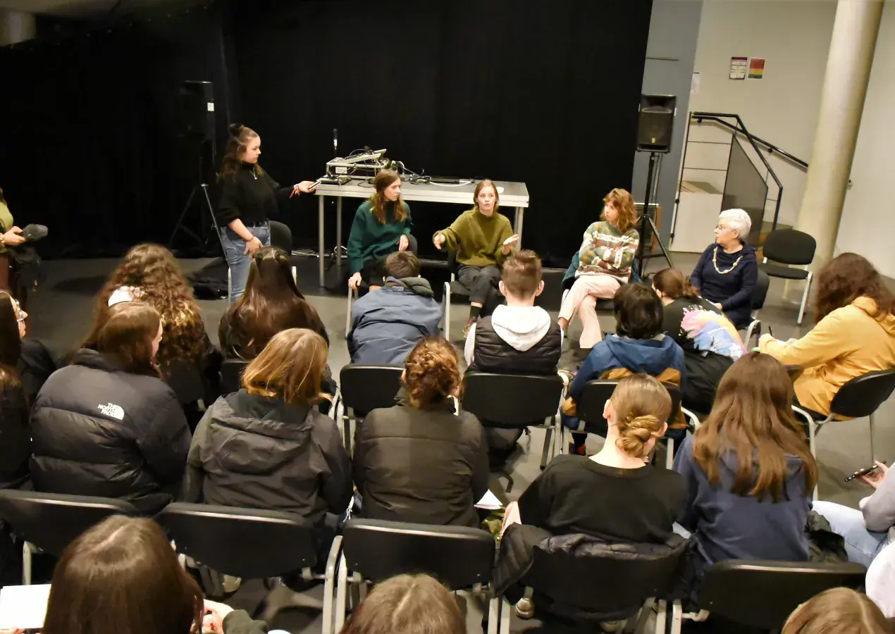 Des artistes échangent dans une salle, au milieu d'un public de lycéens.